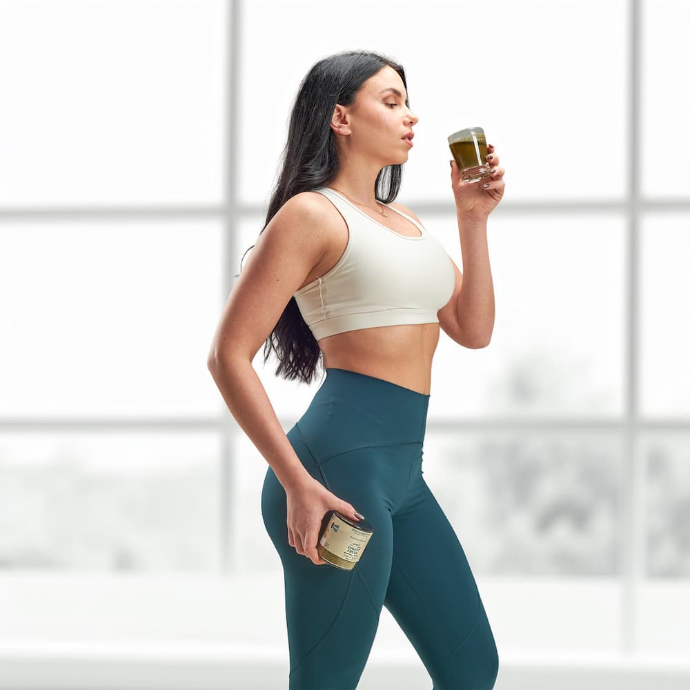 Woman in athletic wear holding a supplement container against a neutral background