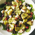 Pesto potato salad with feta, olives, and grapes on a bed of greens.