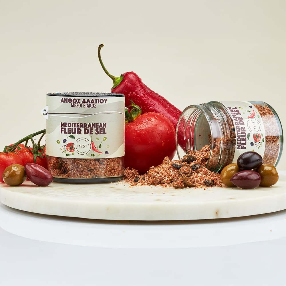 Two containers of Mediterranean Fleur de Sel seasoning on a marble board with vegetables.