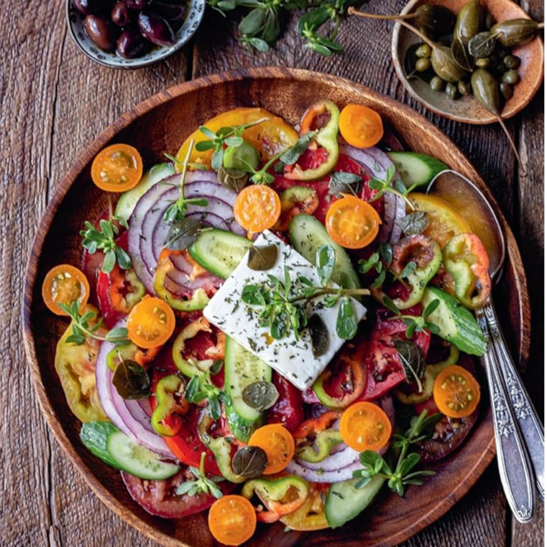 Colorful salad with tomatoes, cucumbers, onions, and feta cheese on a wooden plate.