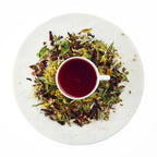 Tea cup with red liquid surrounded by dry tea leaves on a white plate