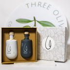 Two bottles in a box with a decorative box labeled 'Three Olives' on a white background.