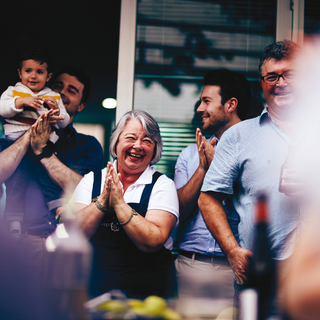 Group of people clapping and smiling, with a woman in the center wearing overalls.