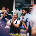 Group of people clapping and smiling, with a woman in the center wearing overalls.