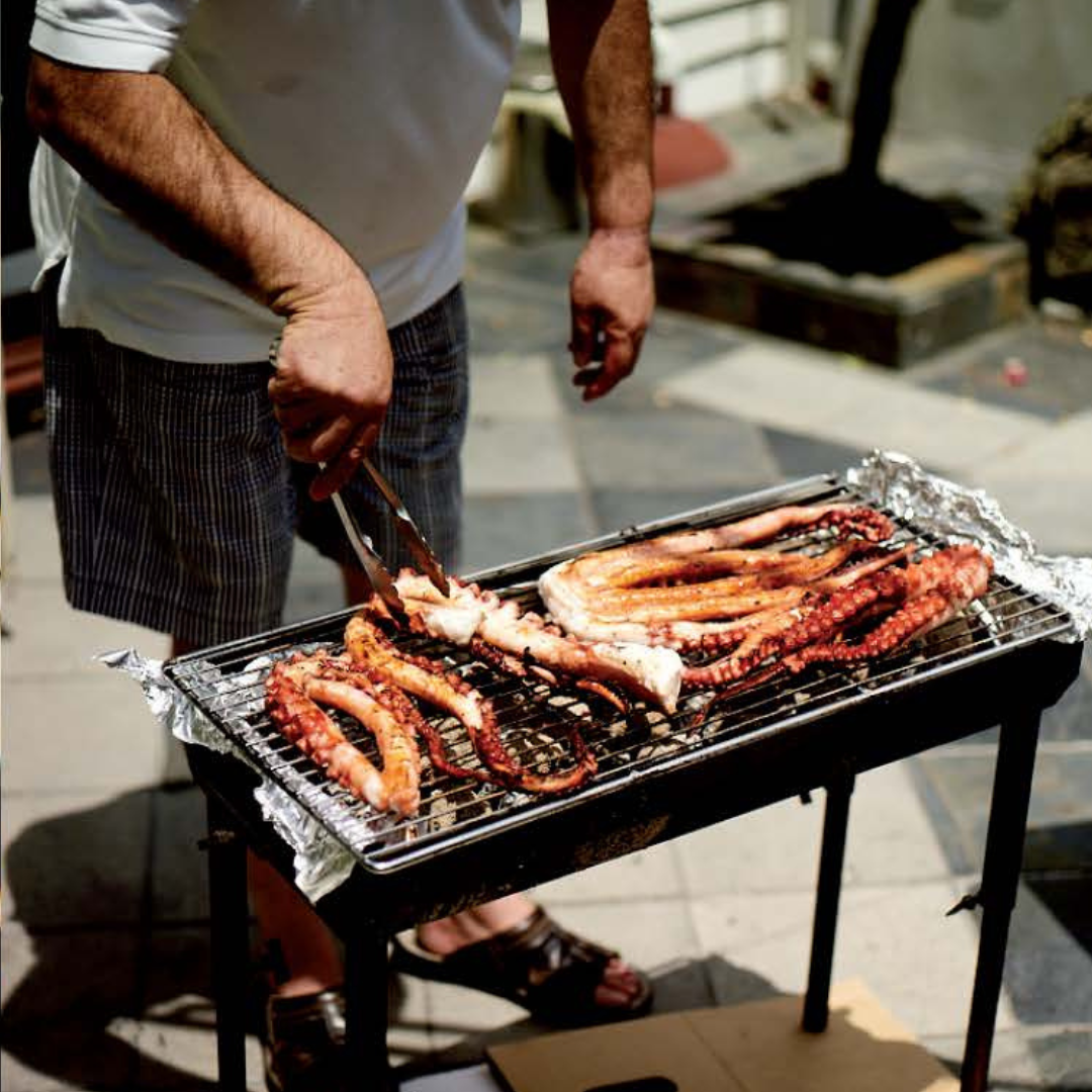 Person grilling octopus on a barbecue grill outdoors.