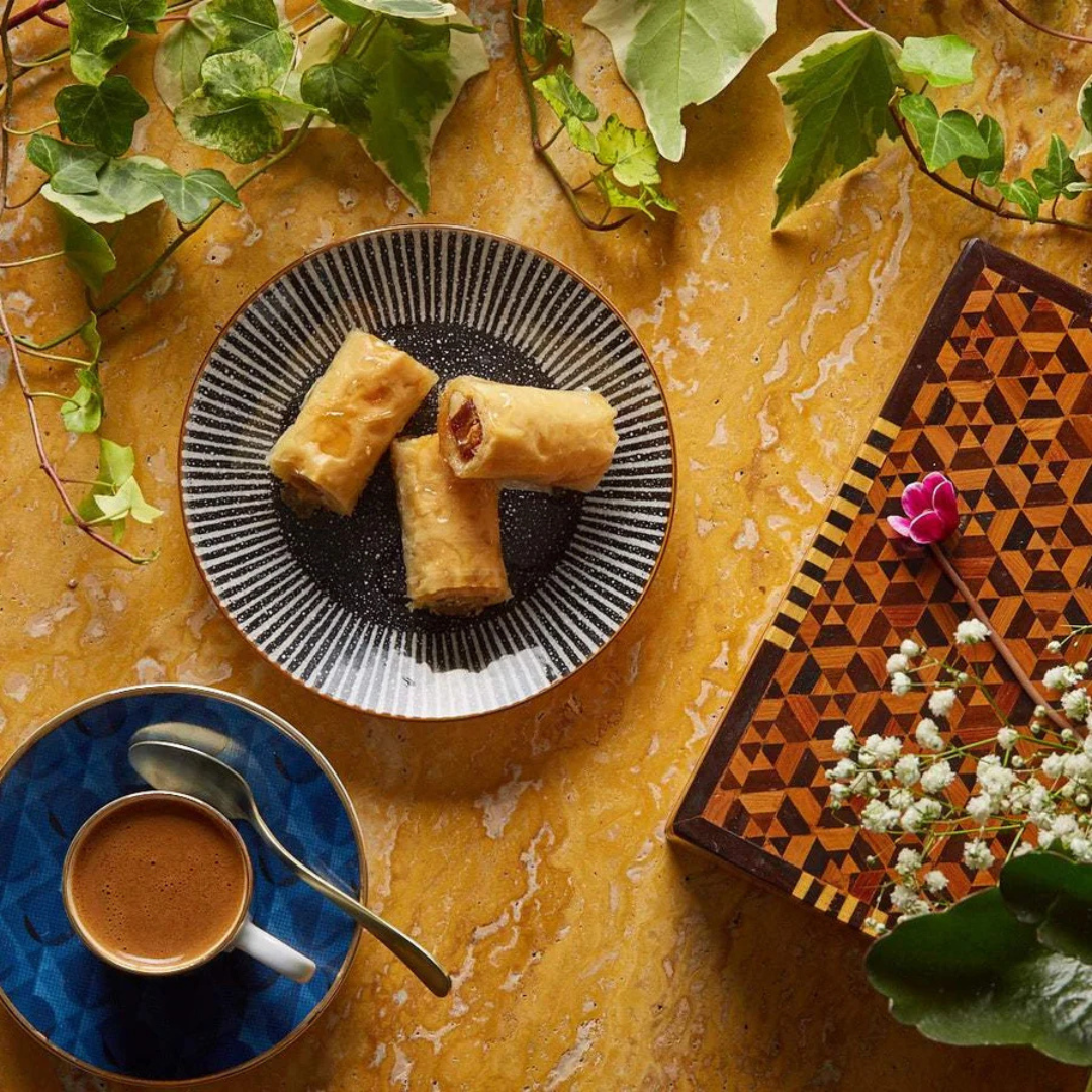Plate of spring rolls on a yellow table with a cup of coffee and decorative elements.