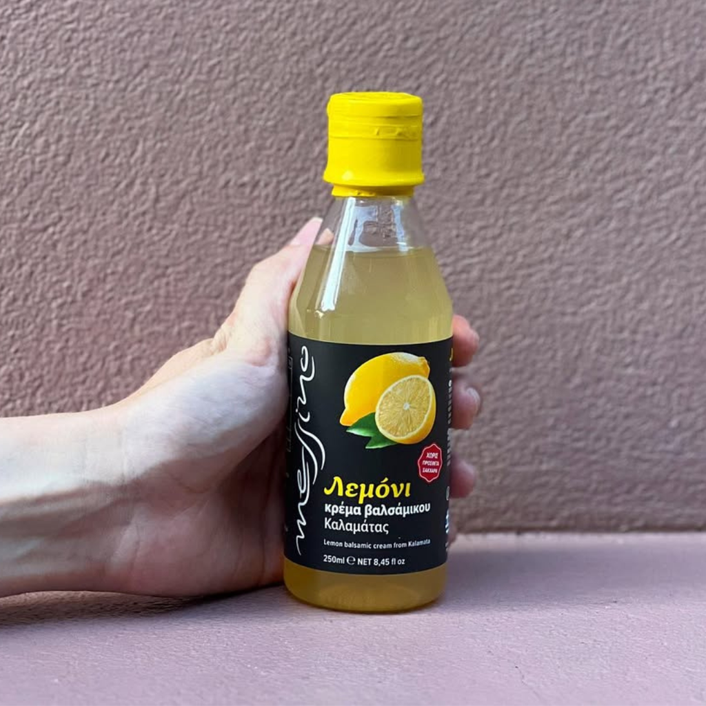 Hand holding a bottle of lemon juice with a yellow cap against a plain background