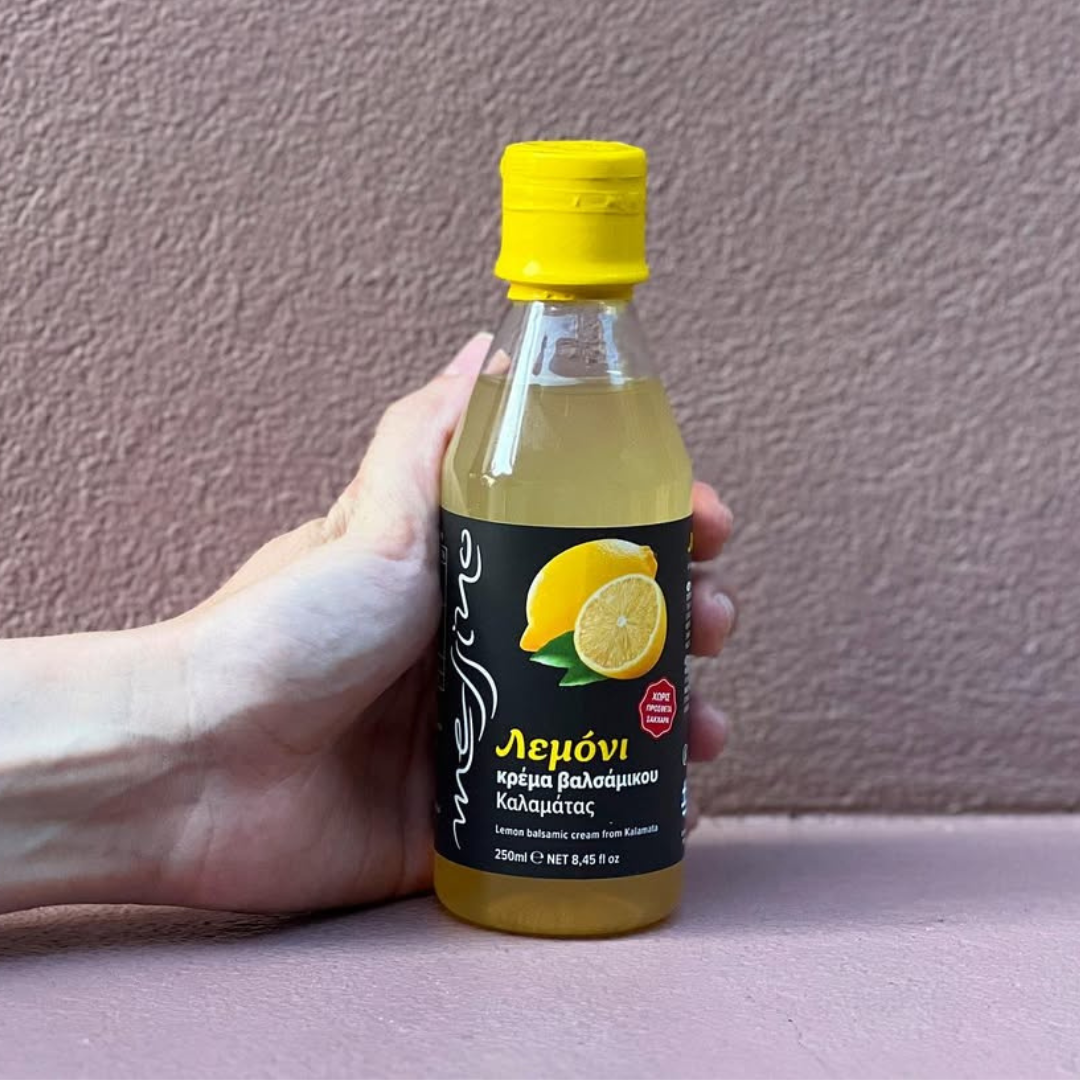 Hand holding a bottle of lemon juice with a yellow cap against a plain background