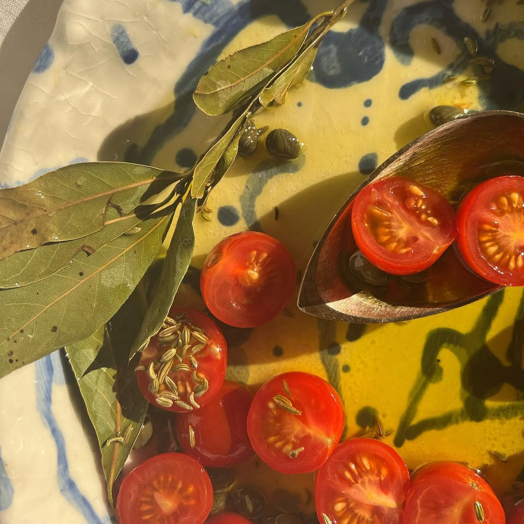 Sliced tomatoes with bay leaves and fennel seeds on a decorative plate.