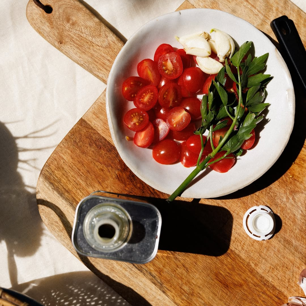 White plate with cherry tomatoes, garlic cloves, and herbs on a wooden surface.
