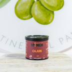 Container of 'The Pinch' Cajun seasoning on a marble surface with green limes in the background.