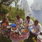 Group of people dining outdoors with a scenic view of the sea and cliffs.