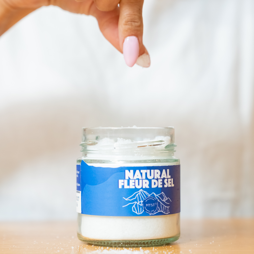 Jar of 'Natural Fleur de Sel' salt with a hand holding it on a blurred background