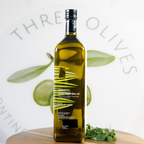 Bottle of olive oil with olive leaves on a white background, featuring the brand 'Three Olives'.