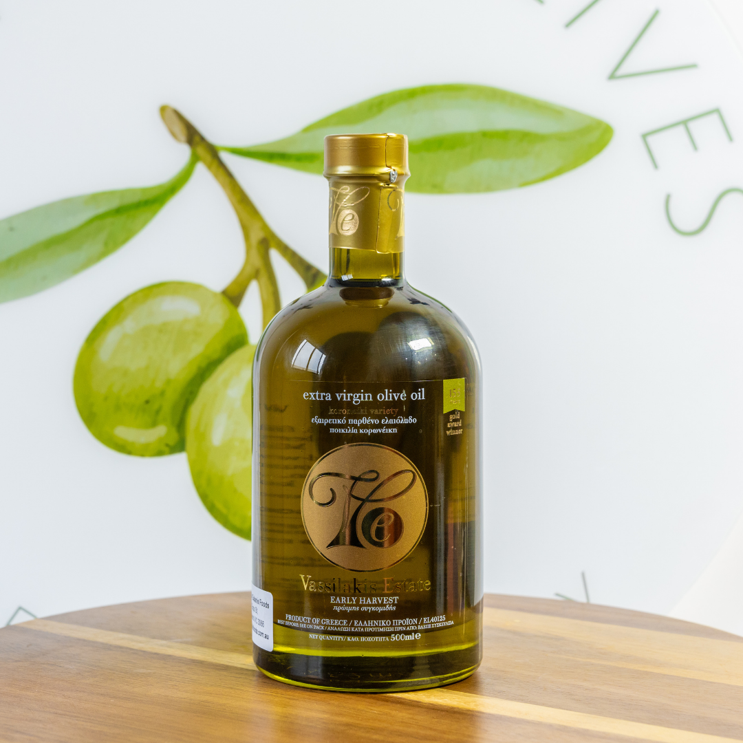 Bottle of extra virgin olive oil on a wooden surface with green olives in the background