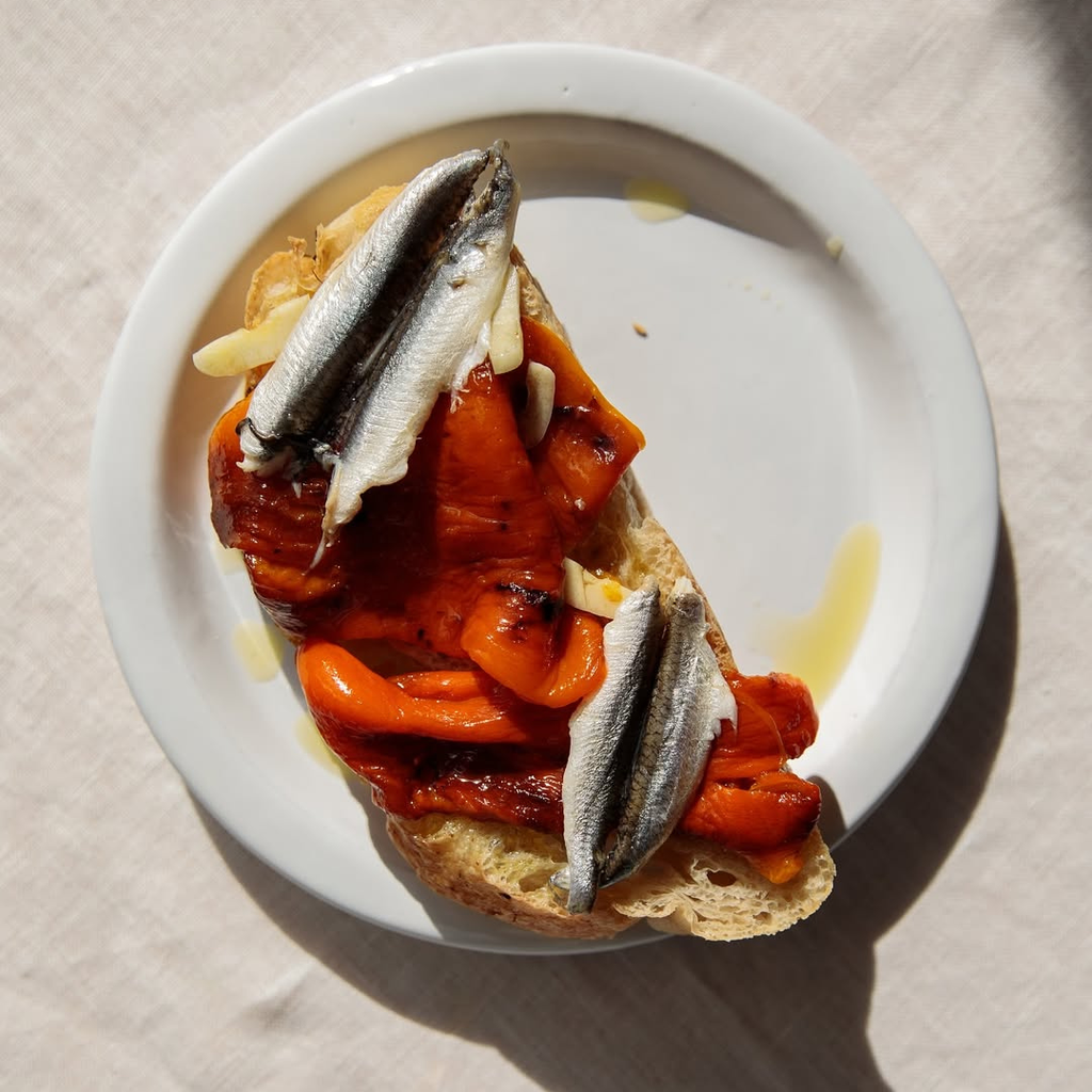 Plated dish with bread topped with roasted peppers and fish on a beige background