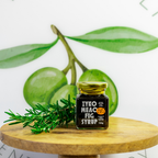 Jar of EYKO MEAO FIG SYRUP on a wooden surface with green figs and rosemary in the background.