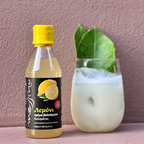 Bottle of lemon cream with a yellow cap next to a glass of lemonade on a pink background