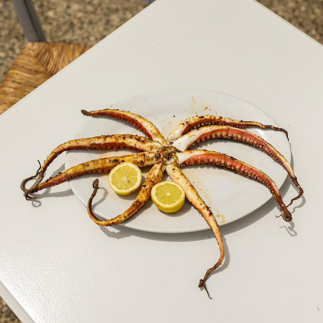 Grilled octopus on a white plate with lemon wedges on a textured surface