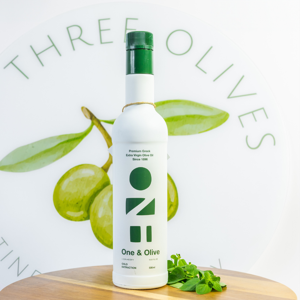 Bottle of One & Olive olive oil on a wooden board with green olives and leaves, branded 'Three Olives'.