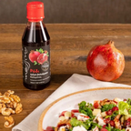 Bottle of pomegranate syrup on a wooden table with a pomegranate and salad.