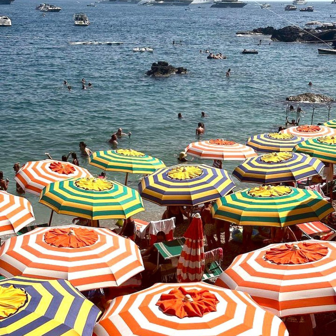Colorful striped umbrellas on a beach with people and boats in the water.