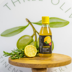 Bottle of lemon balsamic vinegar on a wooden board with lemons and herbs, against a light background.
