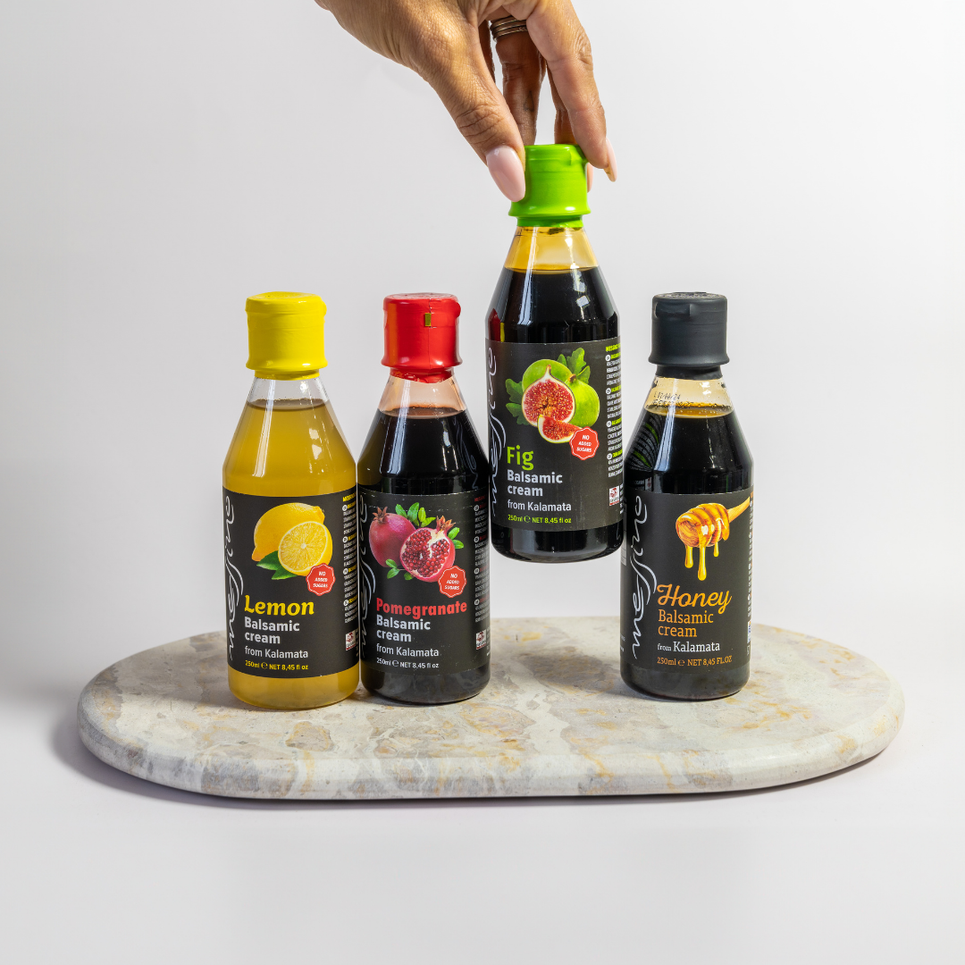 Four bottles of balsamic vinegar with colorful labels on a marble board.