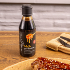 Bottle of honey on a wooden table with food and cutlery in the background