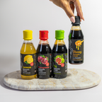Four bottles of balsamic vinegar with colorful lids on a marble surface.