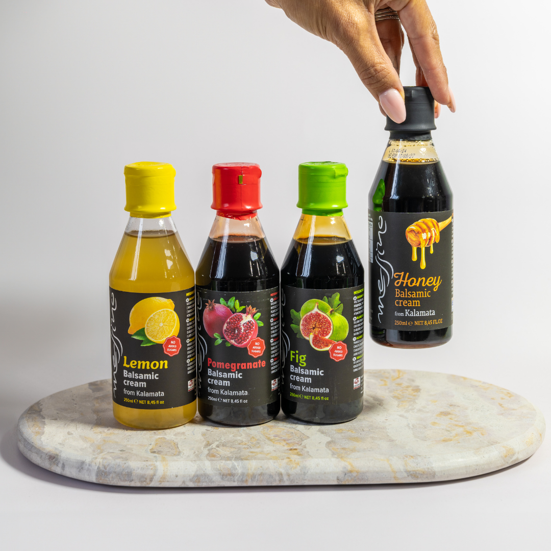 Four bottles of balsamic vinegar with colorful lids on a marble surface.