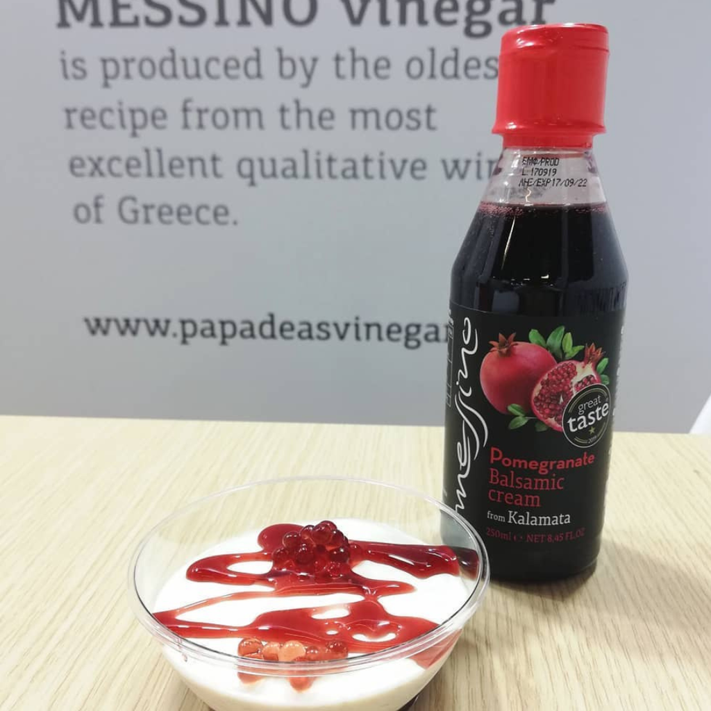 Bottle of Pomegranate Balsamic cream with a bowl of dessert on a table.
