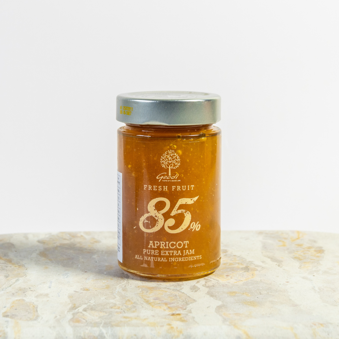 Jar of apricot jam with a visible brand logo on a light marble surface
