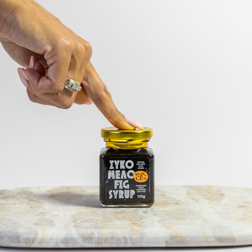 Person opening a jar of ZYKO Mecc Fig Syrup on a marble surface.