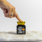 Person opening a jar of ZYKO Mecc Fig Syrup on a marble surface.