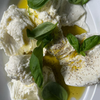 Plated dish of creamy white food with basil leaves and olive oil