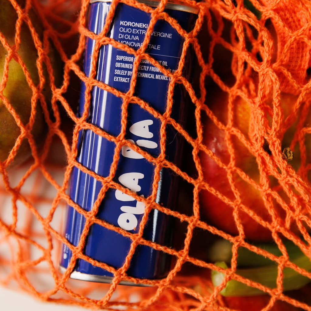 Koroneiki olive oil bottle in an orange mesh bag with fruits