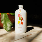 White bottle with colorful 'Olea' branding on a tiled surface with a leaf in the background