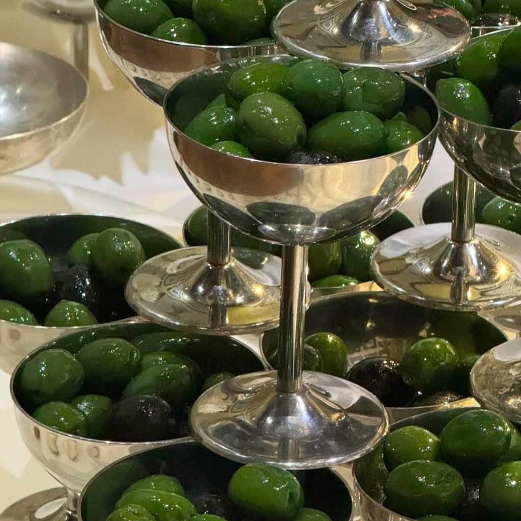 Silver bowls filled with green olives on a reflective surface