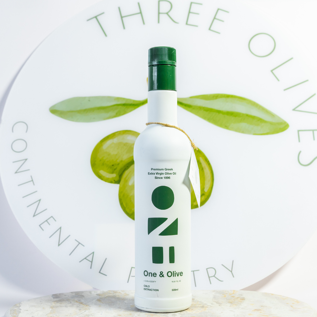 Bottle of olive oil with green leaves and 'Three Olives' branding on a light background