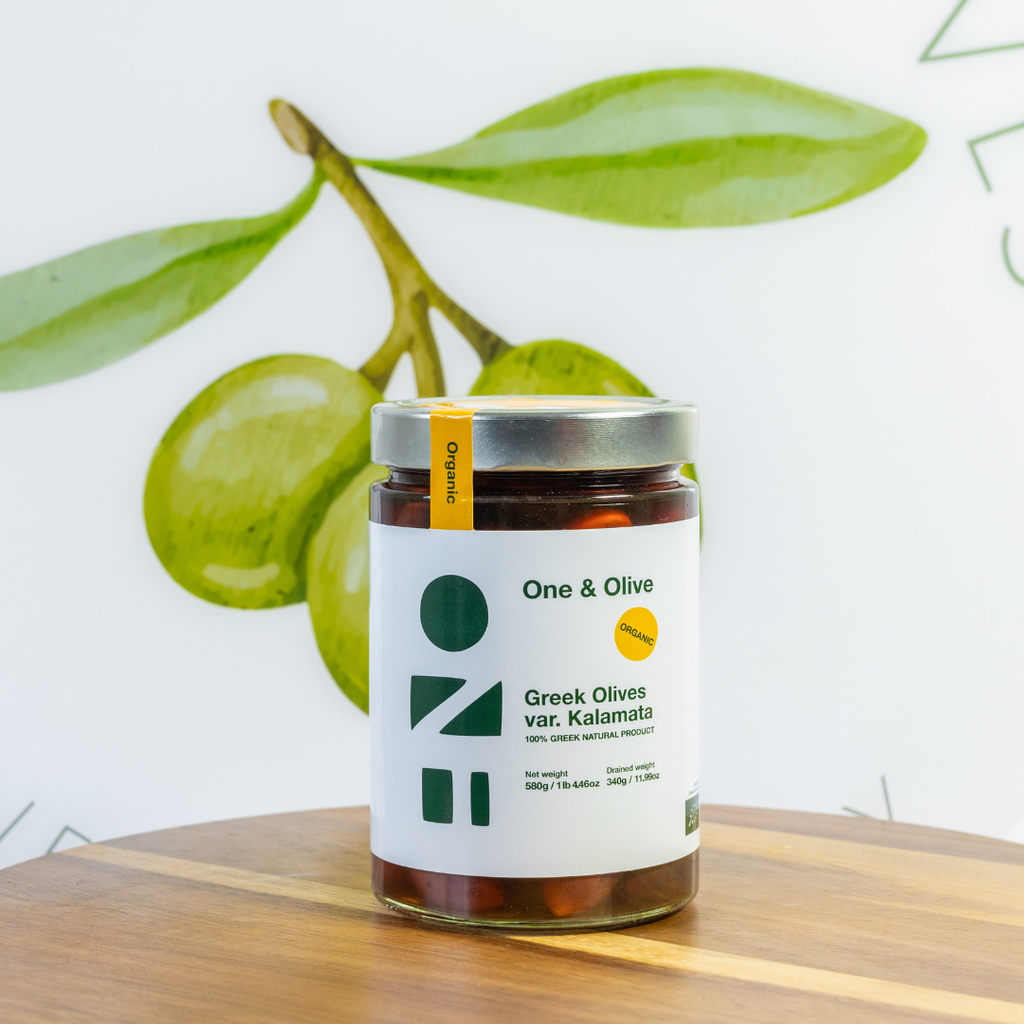 Jar of Greek olives with a label on a wooden surface and green leaves in the background