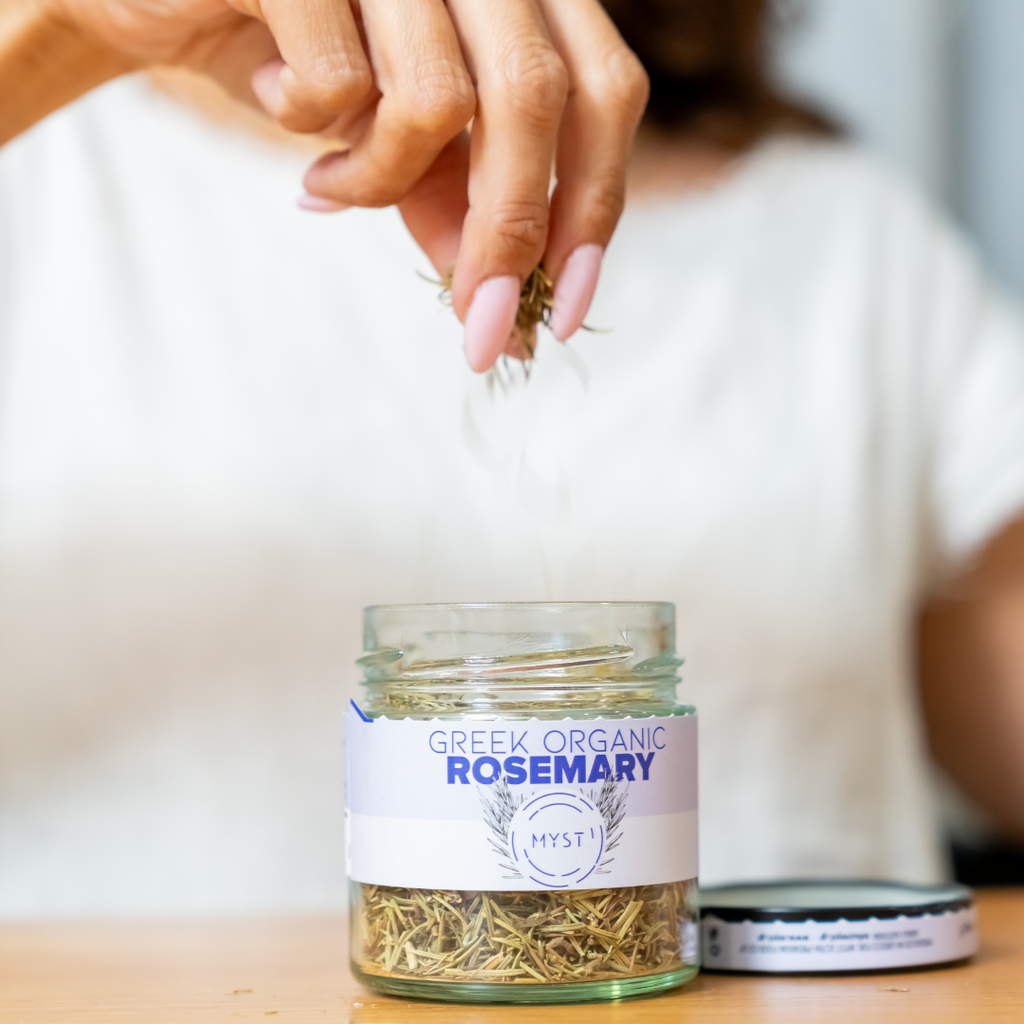 Glass jar labeled 'Greek Organic Rosemary' with a hand holding rosemary leaves.