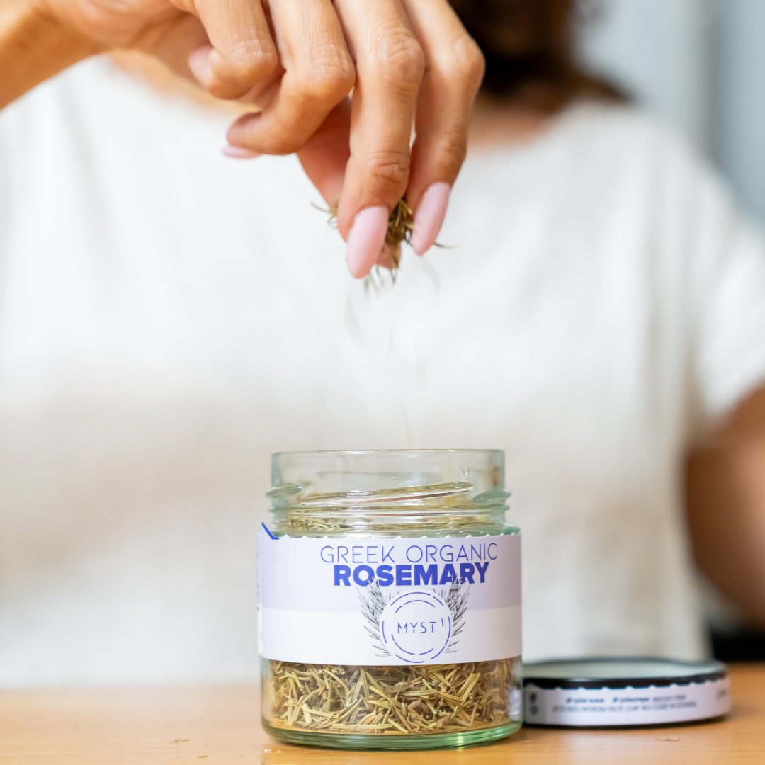 Glass jar labeled 'Greek Organic Rosemary' with a hand holding rosemary leaves.