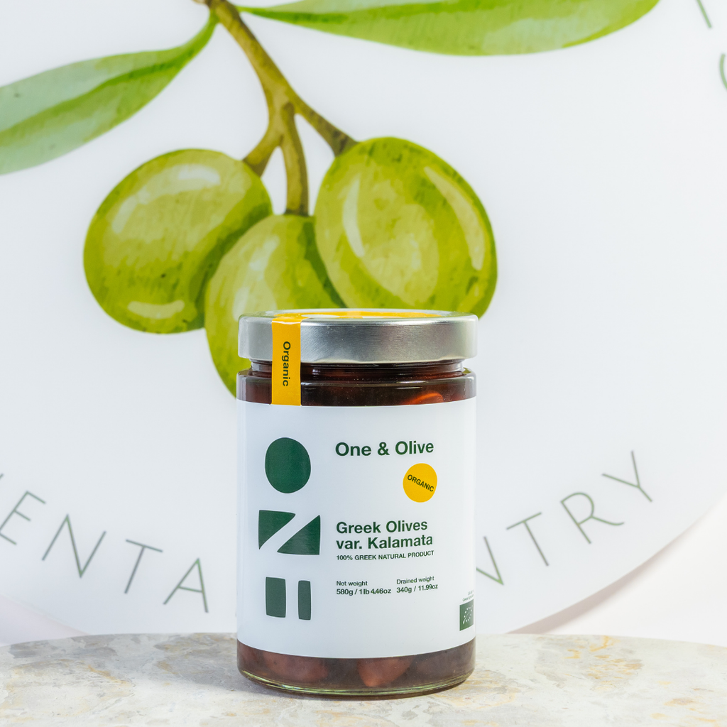 Jar of Greek olives with a One & Olive label, green olives in the background.