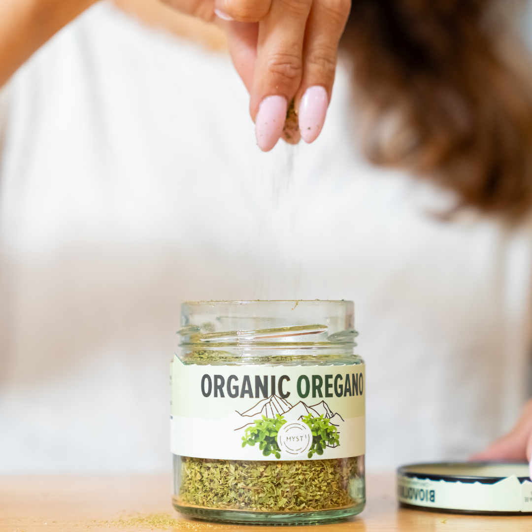 Person adding organic oregano to a jar on a wooden surface