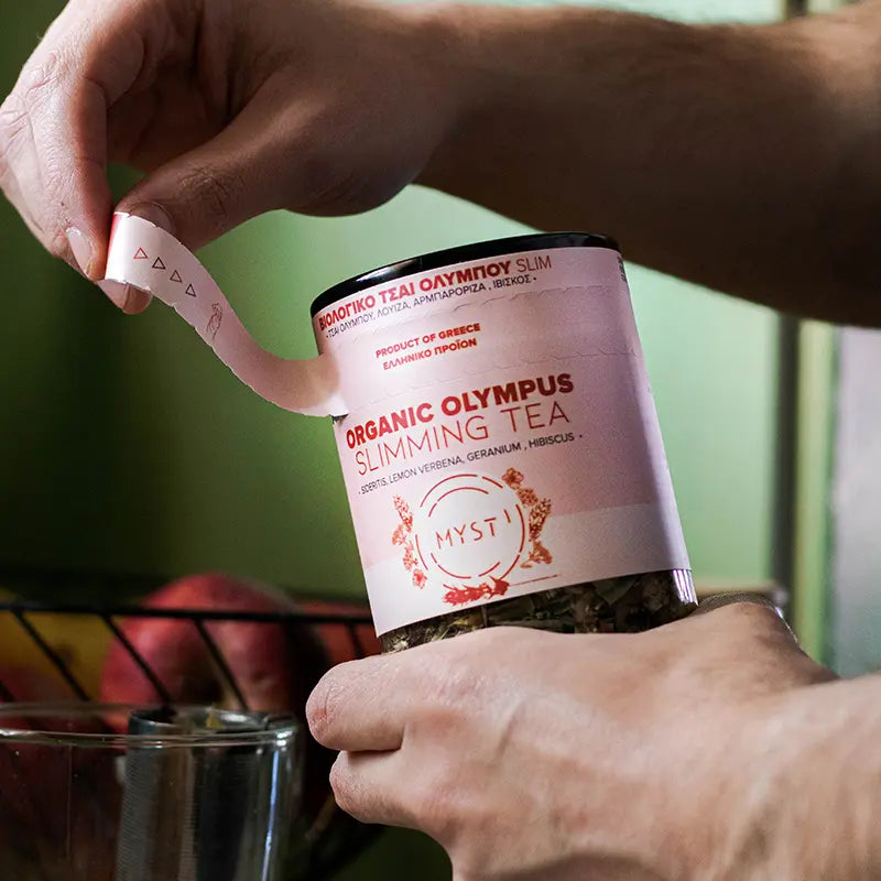 Person holding a container of Organic Olympus Slimming Tea with a blurred background