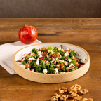 Salad with greens, nuts, and pomegranate seeds in a bowl on a wooden table.