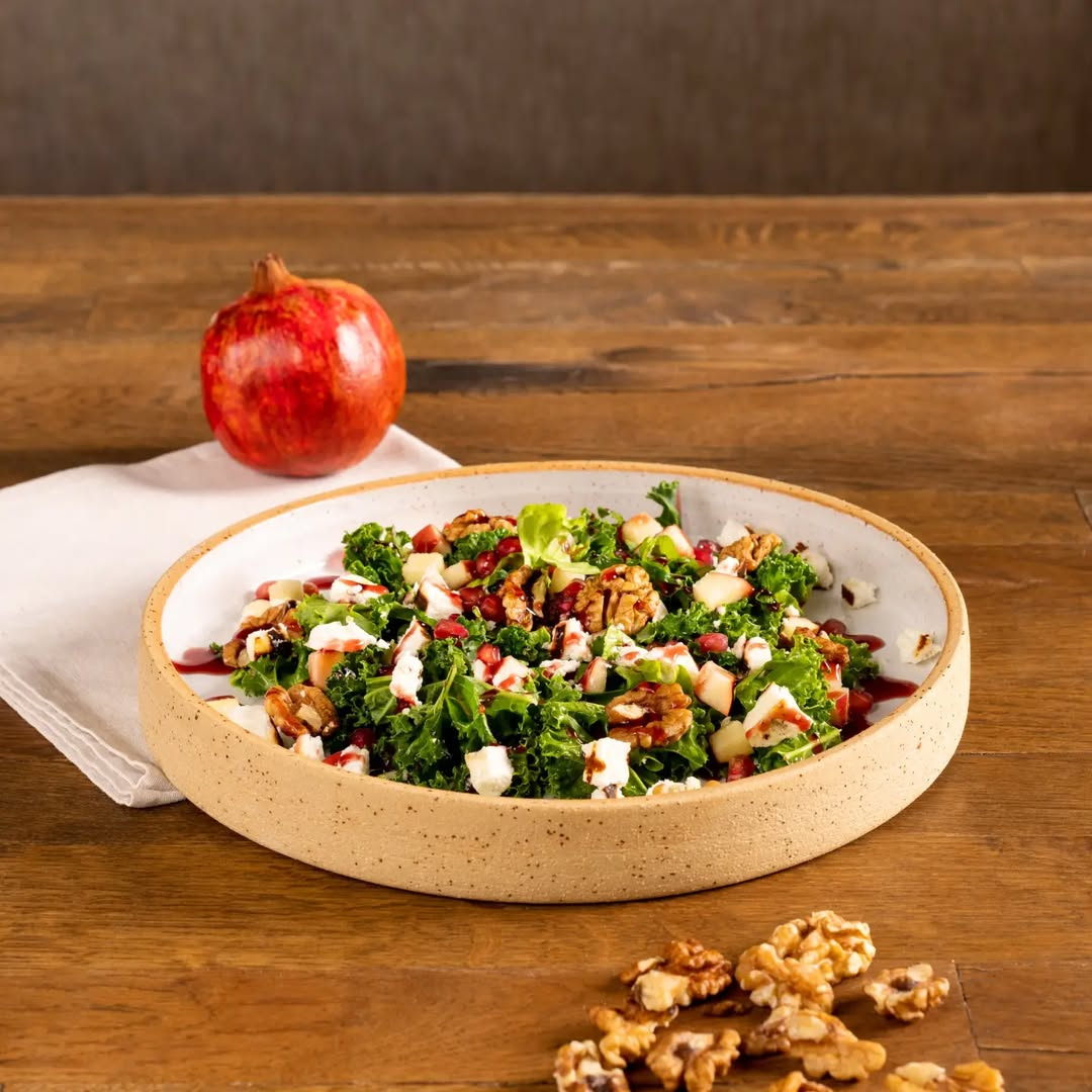 Salad with greens, nuts, and pomegranate seeds in a bowl on a wooden table.
