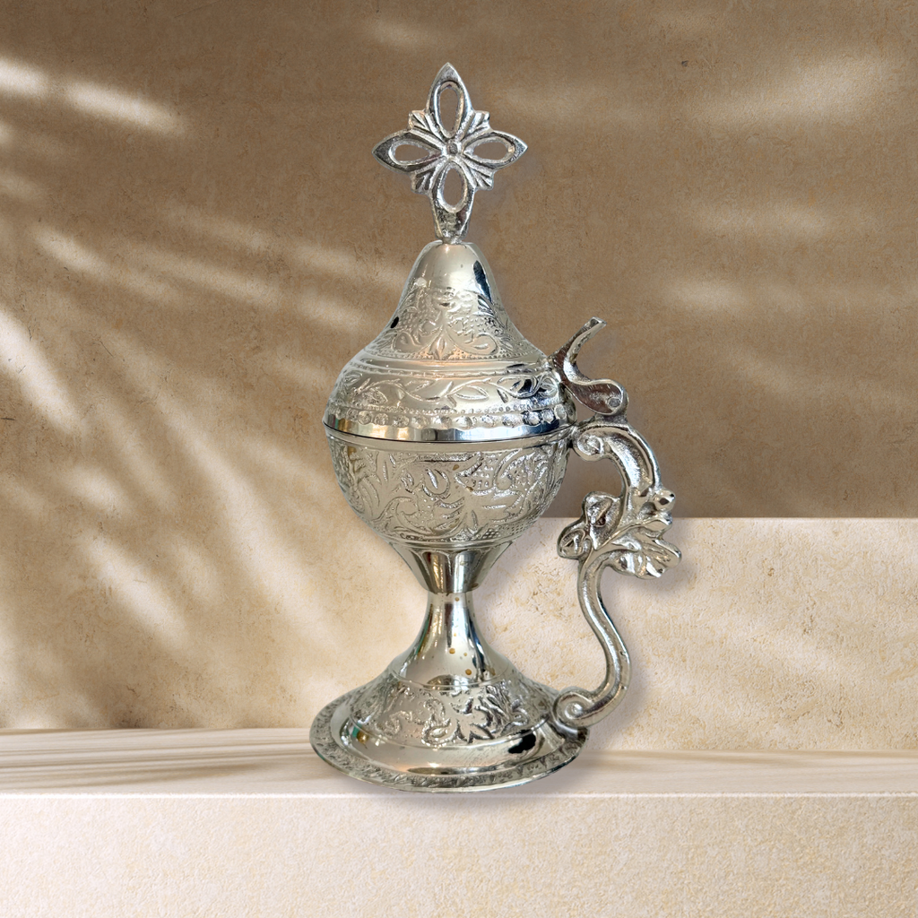 Silver decorative container with intricate designs on a beige surface