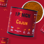 Red container of 'The Pinch Cajun' seasoning with a close-up of the spice on a red background.